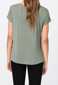 Olivgrön kortärmad skjorta med rund halsringning och böjd fåll, tillverkad i ett slätt, lätt tyg, bärs med svarta byxor.