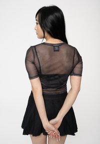 Black sheer top with short sleeves, semi-transparent fabric, fitted design and a tag on the back. Paired with a black flared skirt.