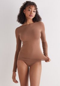 Brązowa bluzka z długim rękawem wykonana z elastycznej tkaniny, dopasowany krój, z lekkim dekoltem w łódkę i bezszwowymi krawędziami, zestawiona z dopasowanymi spodniami.