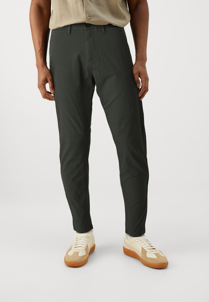 Pantaloni slim-fit verde scuro realizzati in materiale leggero. Presentano un design classico con una texture liscia e passanti per la cintura.