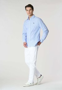 Camicia button-up a righe azzurro chiaro con maniche lunghe, abbinata a pantaloni bianchi e sneakers bianche. Presenta un piccolo logo sul petto.