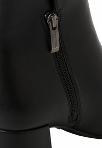 Bottine noire en cuir avec une finition texturée, dotée d'une fermeture éclair latérale en métal argenté et d'un talon épais pour plus de stabilité.