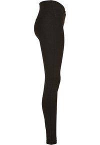 Leggings noirs taille haute en tissu extensible, silhouette ajustée, design sans couture sur les côtés et texture lisse.
