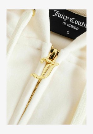 Witte Juicy Couture hoodie met gouden ritssluiting in de vorm van een gestileerde letter "J" en zichtbaar merkembleem aan de binnenkant van de kraag.