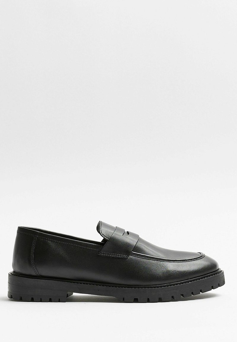 Mocassin en cuir noir avec semelle épaisse en caoutchouc et couture moc toe, profil latéral sur fond blanc.
