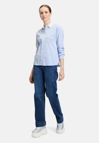 Camicia button-up a righe blu chiaro con colletto bianco, abbinata a jeans blu scuro e sneakers massicce iridescenti.
