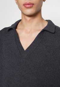 Pull en tricot gris foncé avec un col en V et un col classique. Tissu texturé avec un motif à côtes et un design sans ornements.