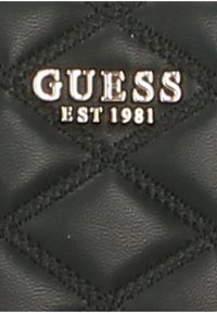 Pelle nera trapuntata con motivo a diamante. Presenta il logo metallico "GUESS" e "EST 1981" in bianco, evidenziando l'identità del marchio.