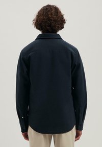 Granatowa koszula z długim rękawem o miękkiej fakturze, z kołnierzykiem, mankietami na dwa guziki i zaokrąglonym hemem. Widok z tyłu, bez widocznych wzorów.