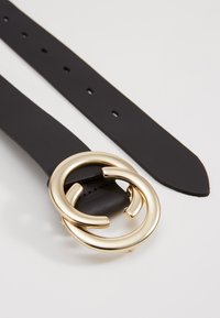 Black leather belt with a circular gold-tone metal buckle featuring two interlocking rings. Smooth texture with multiple adjustment holes.