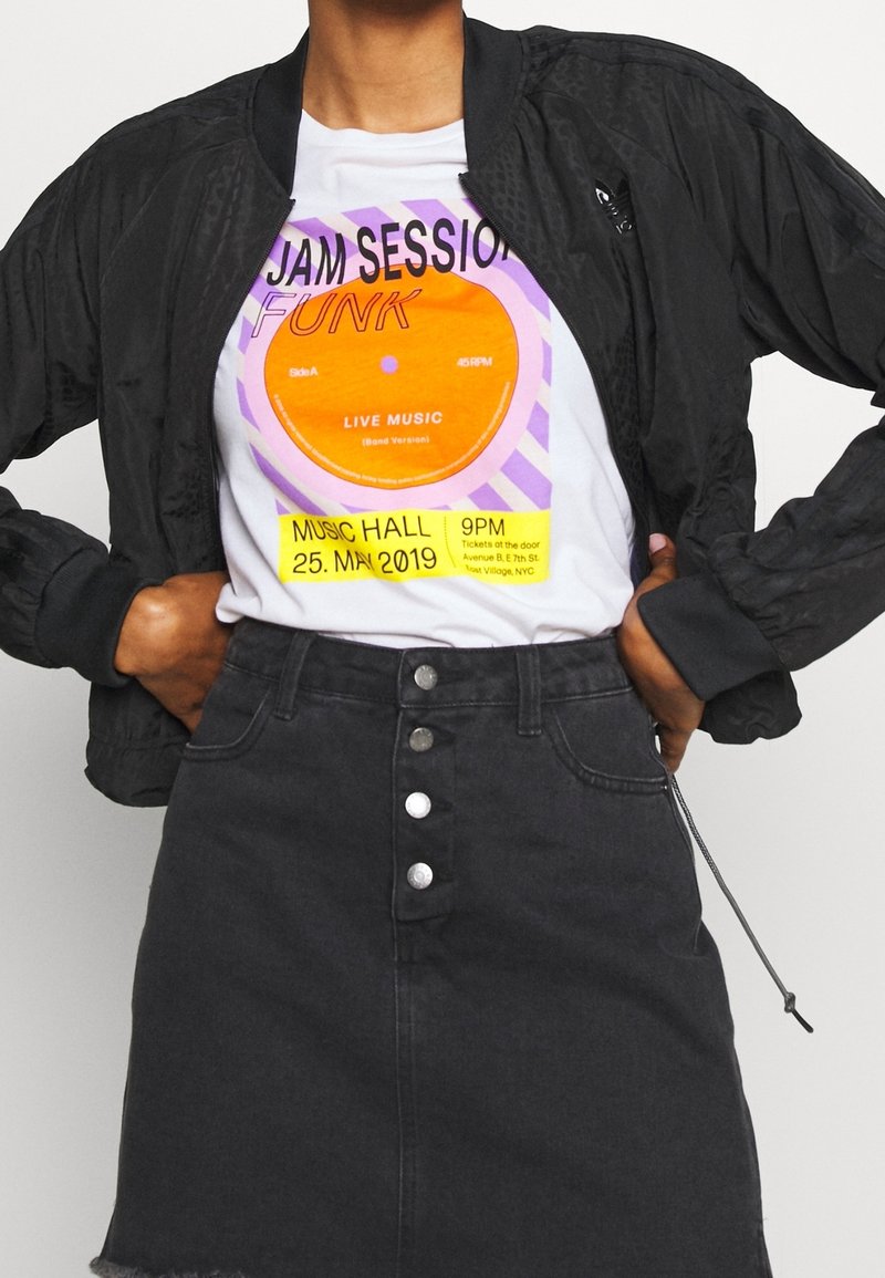 Svart bomberjacka, vit t-shirt med färggrafisk design och text, samt svart denimkjol med synliga knappar och fransat nederkant.