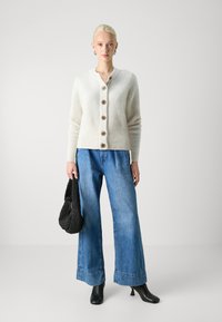 Cream cardigan with six brown buttons, ribbed texture, paired with wide-leg blue denim jeans, black leather ankle boots, and a black bag.