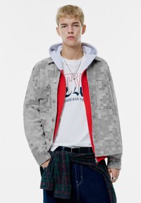 Grå mønstret jakke over en rød hættetrøje, båret med en hvid grafisk t-shirt. Blå jeans og en grønternet skjorte knyttet om taljen. Sølvtilbehør.