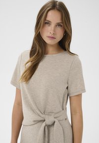 Svetlo béžové šaty tričkového strihu s krátkymi rukávmi, okrúhlym výstrihom a detailom uzla v páse. Mäkka, hladká textúra so subtílnym melírovaným vzorom.