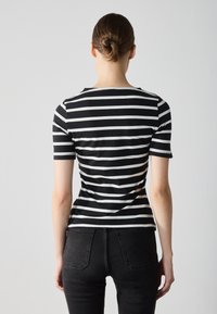 Black and white striped short-sleeve top with a round neckline. The fabric is soft and fitted, worn with high-waisted dark jeans.