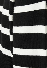 Gros plan sur un tissu tricoté à rayures horizontales noires et blanches montrant les détails de texture et de motif.