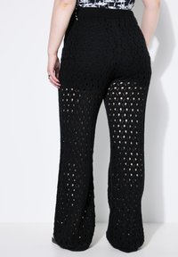 Zwarte wijde gebreide broek met een open breipatroon, elastische tailleband en een zachte textuur die het licht vangt en een vloeiende uitstraling creëert.