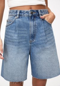 Szorty dżinsowe w jasnoniebieskim kolorze z wysokim stanem, posiadające zapięcie na guzik, szlufki na pasek oraz surowy dół z postrzępionymi brzegami. Dwie boczne kieszenie.