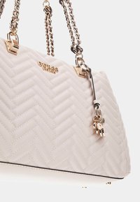 Borsa a tracolla trapuntata color beige chiaro con motivo a zigzag, accessori in tonalità oro, manici a catena e un ciondolo decorativo. Texture in pelle liscia.