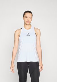 Top sportiv alb fără mâneci, cu decolteu rotund, având accente de logo negre. Material ușor, cu o textură netedă. Asortat cu colanți negri.