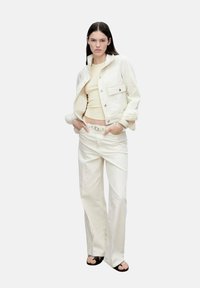 White denim jacket over a light yellow top, paired with high-waisted white pants. Includes a simple belt and flat black sandals.