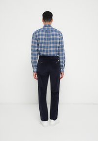 Geruite blauwe shirt met lange mouwen, gecombineerd met donkere marineblauwe corduroy broek. Witte sneakers maken de outfit af. Zichtbare achterkant details van de kleding.