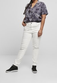 Jeans bianchi attillati con tasche frontali, abbinati a una blusa a maniche corte di colore viola scuro con effetto tie-dye e sneakers alte nere.
