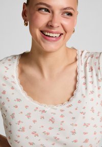 Witte geribbelde top met een bloemendessin in roze en groen, met een geschulpte kantenkraag en korte mouwen.