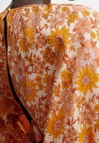 Tissu à motifs floraux dans des tons chauds d'orange et de jaune, arborant de grandes marguerites et de petites fleurs détaillées sur un fond clair.