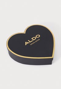 Černá srdcovitá krabička se zlatým okrajem, na jejíž horní straně je zlatým písmem vyznačeno "ALDO SPECIAL EDITION".