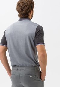 Polo shirt gris à manches courtes avec un col gris foncé, présentant un motif rayé. Porté avec un pantalon gris clair, affichant une coupe décontractée.