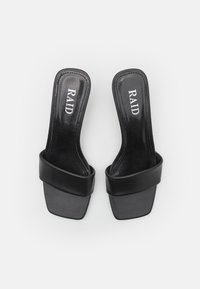 Sandales à talons noirs avec un dessus en simili cuir lisse et une large sangle. Zone des orteils de forme rectangulaire et finition brillante sur la semelle.