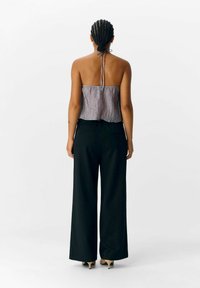 Zwarte wijde broek in combinatie met een losse, gekreukelde lila haltertop. De top heeft een strik achteraan de halslijn voor aanpassing.
