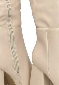 Las botas altas beige presentan un acabado de imitación de cuero suave, un zipper lateral y un tacón grueso para mayor elevación.