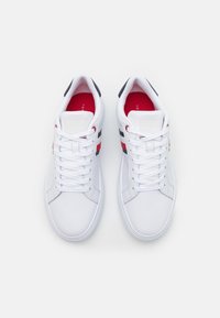 Bílé tenisky s hladkým koženým svrškem, zdobené červenými a námořnickými pruhy. Zavazování na tkaničky a polstrovaný jazyk, s kontrastní červenou stélkou.