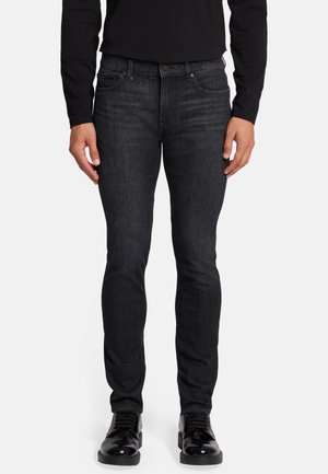 Slim-fit zwarte denim jeans met een licht vervaagde afwerking, vijfzakkenontwerp en metalen klinknagels. G gedragen met zwarte veterschoenen.