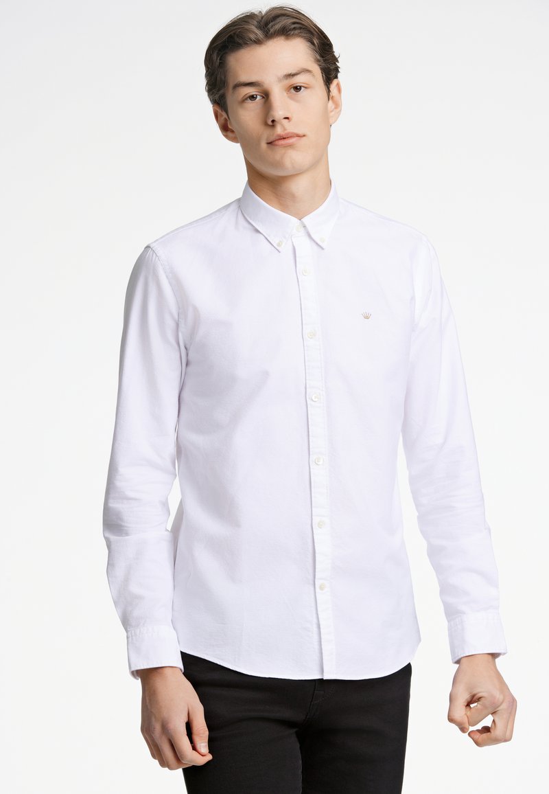 Camisa blanca de botón hecha de algodón con mangas largas, un cuello clásico y un sutil logo bordado en el pecho. Corte entallado, textura suave.
