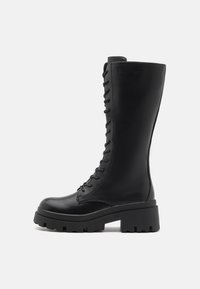 Black leather knee-high boots with a chunky sole. Features front lacing and a smooth texture, providing a sleek and sturdy design.