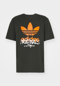 Černé bavlněné tričko s velkým oranžovým logem trefoil a nápisem "adidas ORIGINALS" v bílé kurzívě na přední straně. Krátké rukávy, kulatý výstřih.