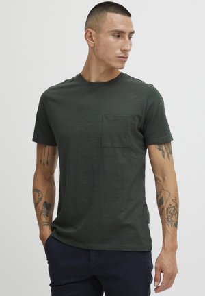 Camiseta de manga corta verde oscuro con cuello redondo y un bolsillo en el pecho. La tela parece suave con un acabado ligeramente texturizado.