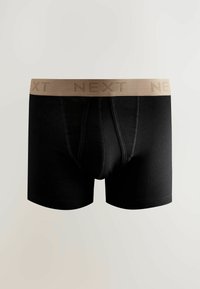 Fekete boxer alsónadrág, világosbarna elasztikus derékpánttal, amelyen a "NEXT" szó ismétlődik. Az anyag simának és rugalmasnak tűnik.