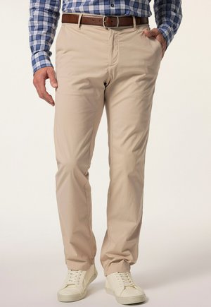 Beige Chinos aus leichtem Stoff. Sie haben einen klassischen Schnitt, Seitentaschen und eine glatte Textur. Kombiniert mit weißen Sneakers.