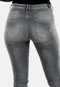 Jeans de denim ajustados en gris claro, que presentan un diseño de cinco bolsillos con acentos bordados y una textura ligeramente deslavada.