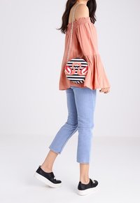 Pyöreä olkalaukku mustavalkoisilla raidoilla, joissa on punaisia flamingo-yksityiskohtia. Hopeinen ketjusovite. Ominaisuuksiin kuuluu sileä pinta.