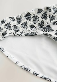 Bikiny spodný diel s čierno-bielym listovým vzorom a volánovým pásom. Mäkka tkanina s hladkým bielym vnútrom a dokončenými okrajmi.