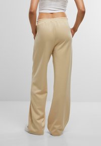 Bežové tepláky s voľným strihom a elastickým pásom, ktoré majú hladkú textúru a široké nohavice, skombinované s bielymi teniskami.