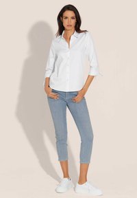 Weißes Hemd mit langen Ärmeln, kombiniert mit hellblauen Skinny-Jeans mit schmalem Schnitt. Getragen mit weißen Sneakers.