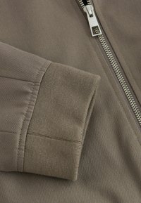 Grau zip-Jacke mit gerippter Textur. Verfügt über einen silbernen Reißverschluss und einen soliden Bund, der einen glatten und strapazierfähigen Stoff zeigt.