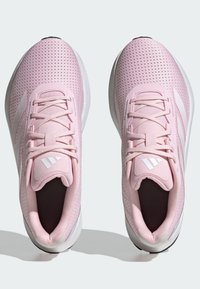 Jasnoróżowe buty sportowe wykonane z materiału siatkowego, z białymi akcentami, teksturowanym wzorem i wyściełanym językiem.
