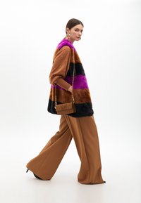 Faux fur vest with purple, black, brown stripes; tan oversized blouse with gold accents; brown wide-leg pants; small brown handbag.